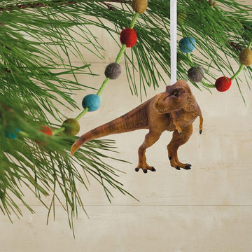 Dinosaur ornament hanging on a Christmas tree with colorful berries.